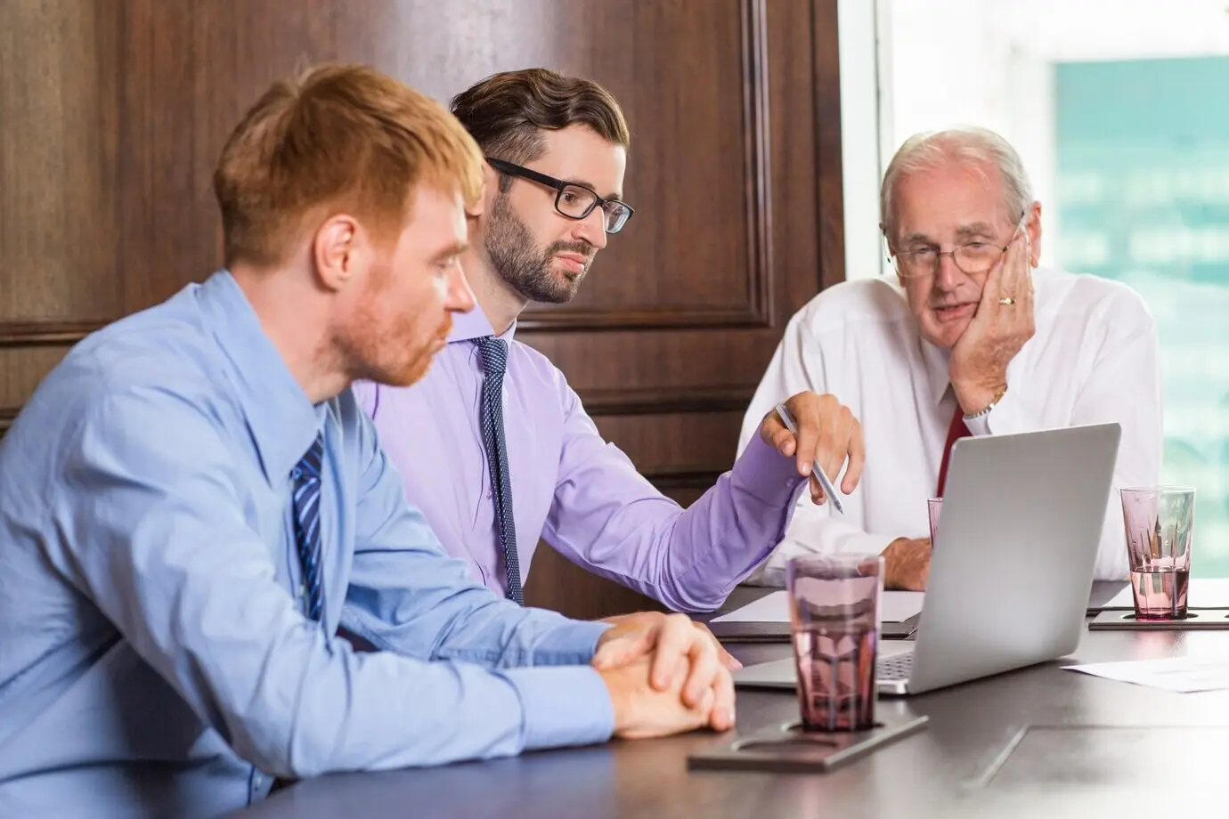 Старший по должности деловой мужчина смотрит на ноутбук другого сотрудника.